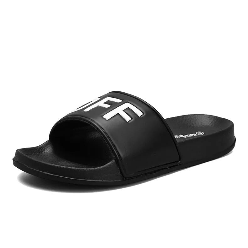A pair of black open-toe men's slippers with a visible rubber sole, shown on a wooden floor.