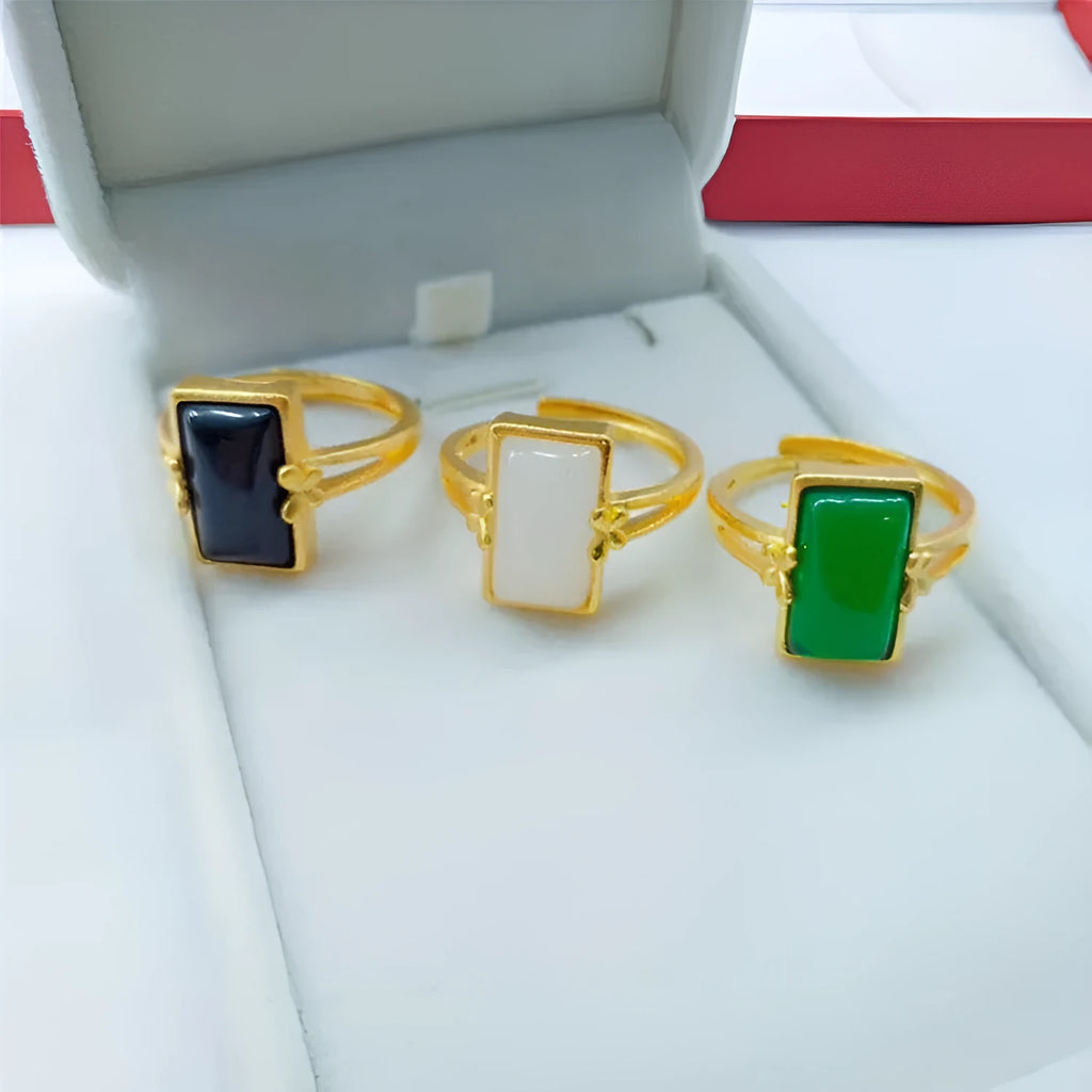 Adjustable gold-plated brass ring with a coloured gemstone inlay on a plain background.