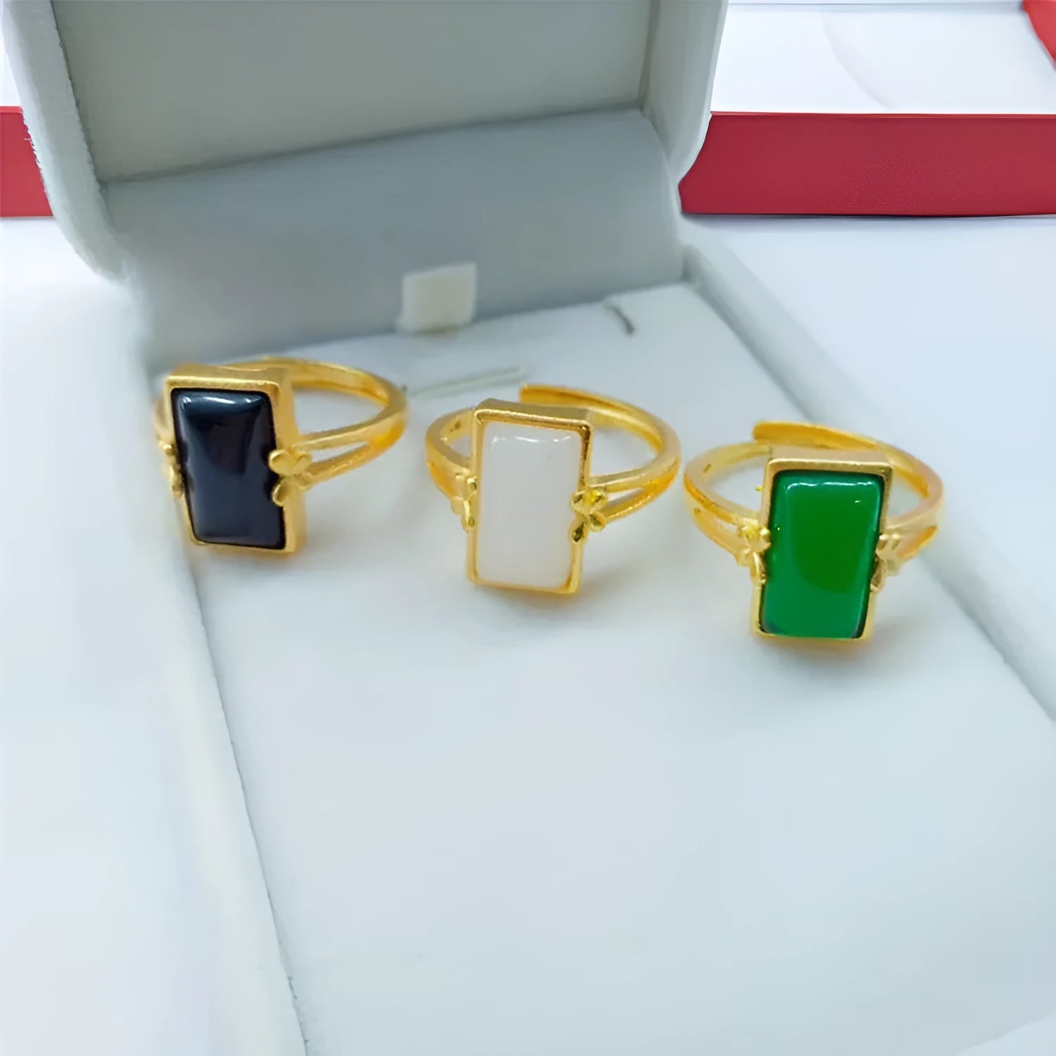 Adjustable gold-plated brass ring with a coloured gemstone inlay on a plain background.