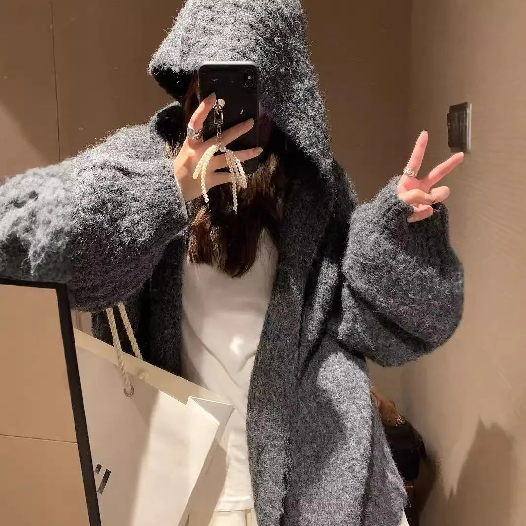 A woman wearing a loose-fit dark grey hooded cardigan made from thick acrylic blend fabric.