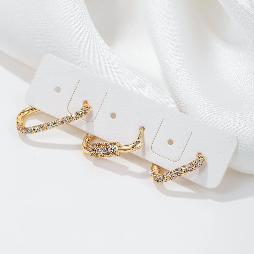 Three geometric copper earrings with inlaid zircon on a square clip, in gold and white finishes.