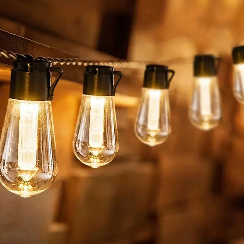 String of retro long infusion bottle shaped outdoor fairy lights hung in a garden.