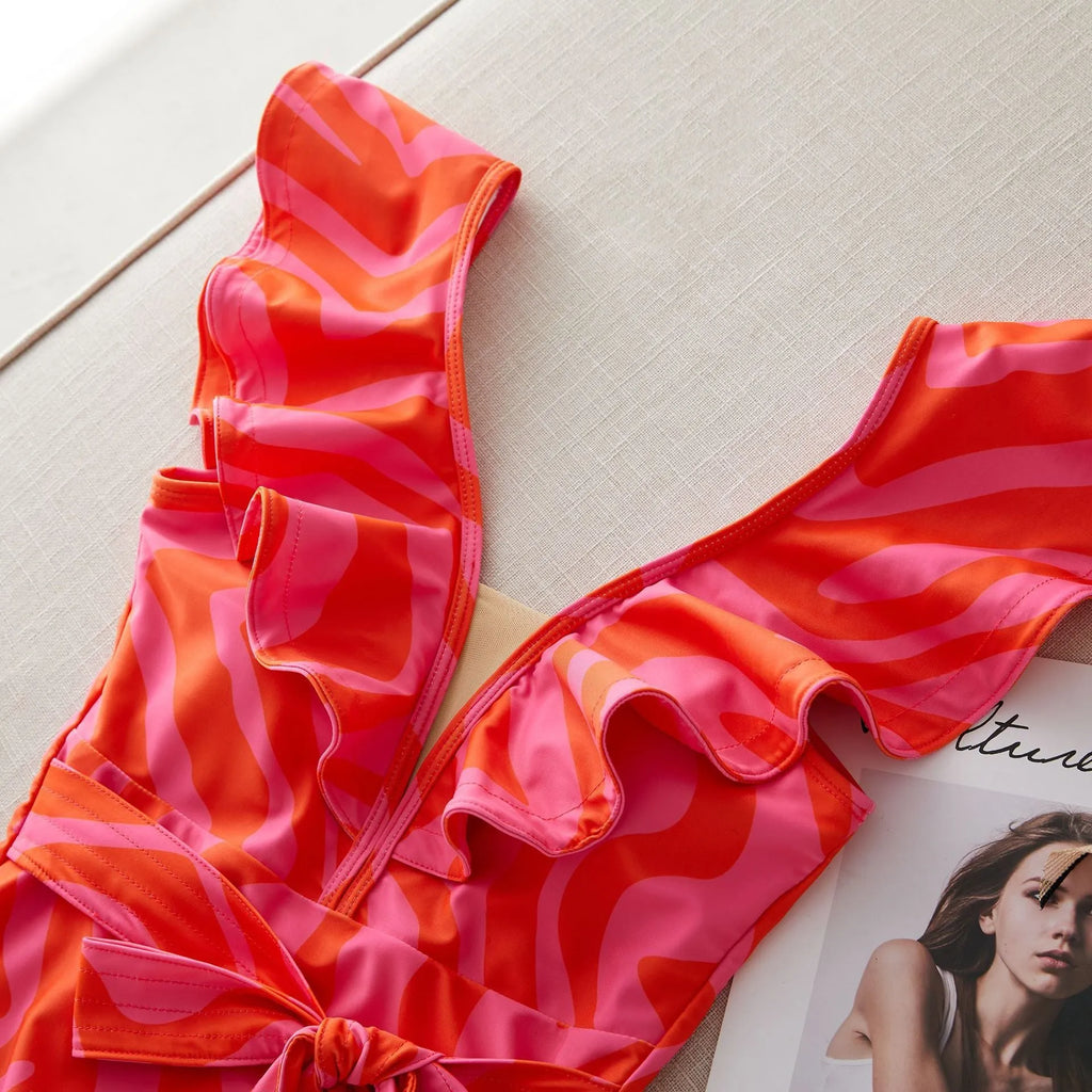 Women's printed one-piece swimsuit with double shoulder straps and ruffled mesh detail on a deep V-neck.
