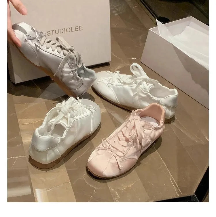 Women's champagne pink satin ballet flats with front lace-up and round toe on a white background.