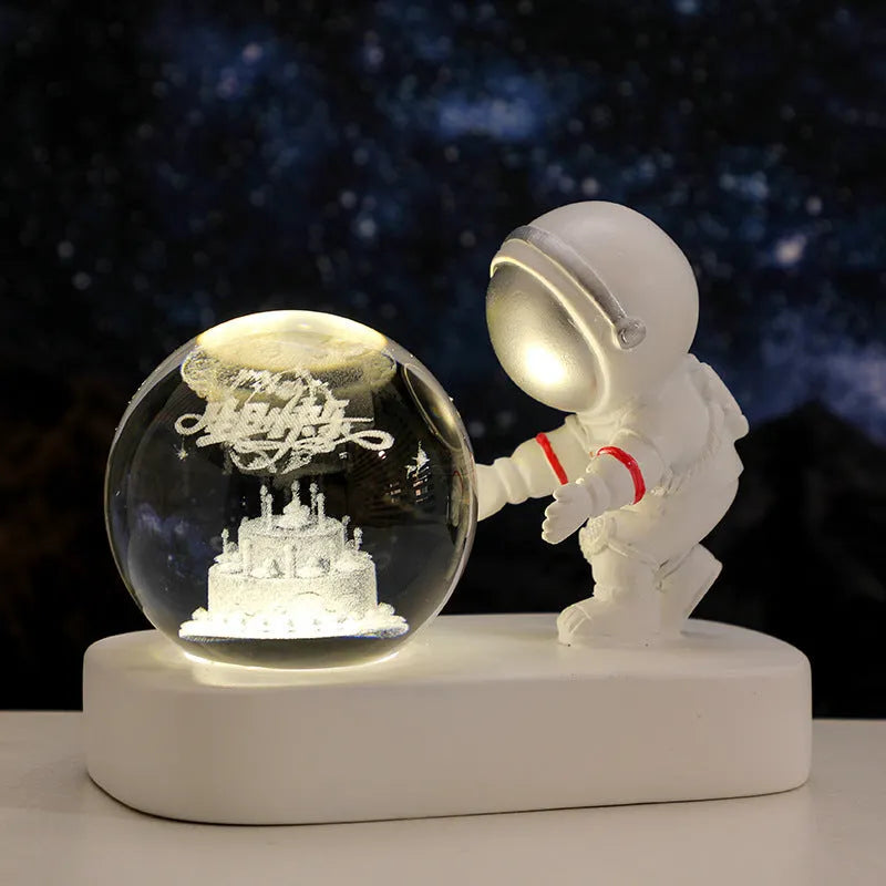 6cm glowing resin crystal ball night light showing an astronaut and planets inside, on a bedside table.