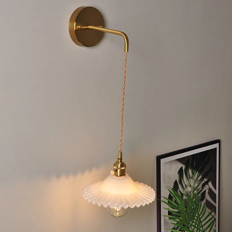 Retro brass-toned copper wall lamp with a white glass lotus shade mounted beside a bed.