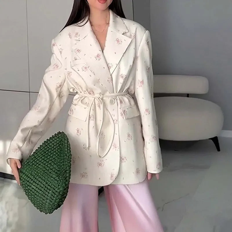 White floral print suit jacket with a lace-up detail at the waist on a hanger.