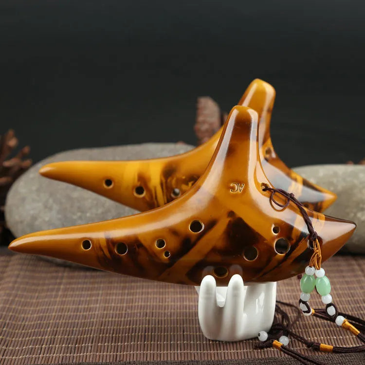 Yellow 12-hole ceramic Alto C ocarina with smoldering finish and lanyard on a surface