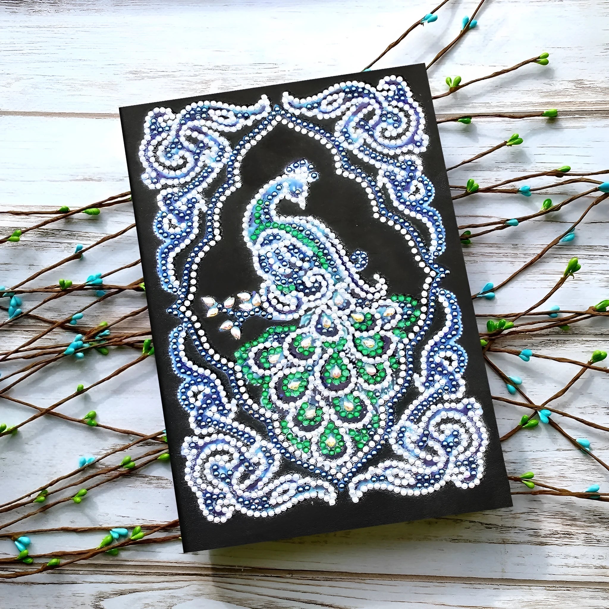 Peacock Beauty A5 diamond painting notebook with coloured resin drills on a black cover.