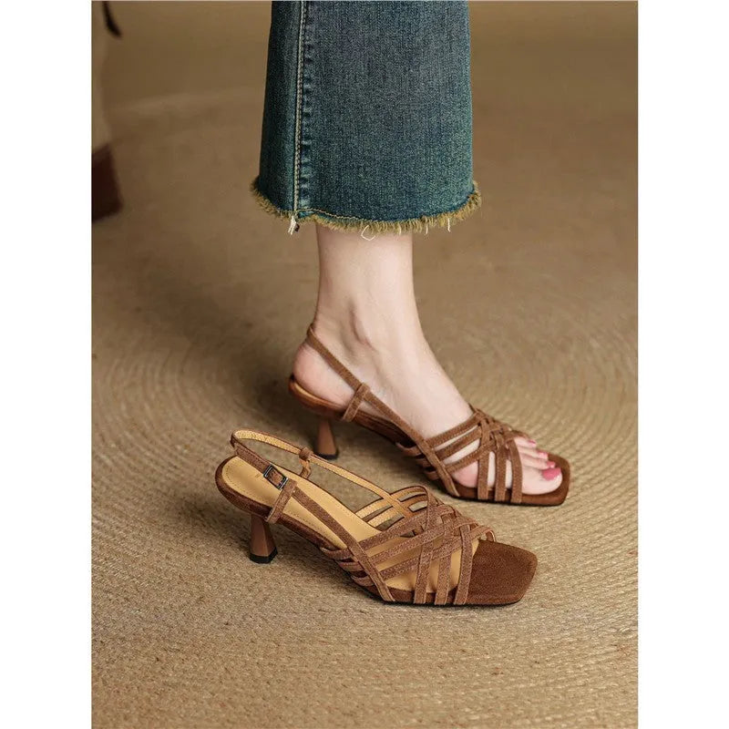 Light brown women's sandals with thin crossing straps and an ankle buckle on a wooden floor.