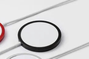 Silver metal Magsafe-compatible magnetic wireless charger for iPhone on a wooden desk.