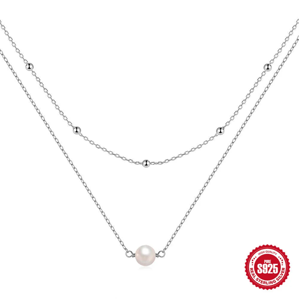 Close-up of a double-layer sterling silver necklace with twin pearl geometric pendants on a ball bead chain.