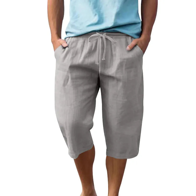 Man wearing loose-fit light khaki linen shorts with a drawstring waist and cropped leg.