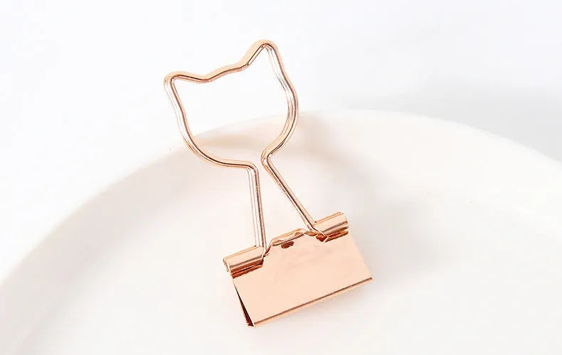 Gold metal alloy paper clip with decorative bow shape top on white background.