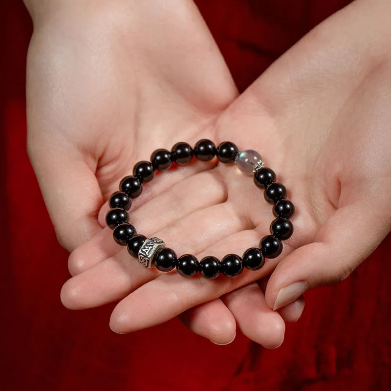 Obsidian bead bracelet with a hand-carved zodiac animal and bodhisattva charm on a wrist.