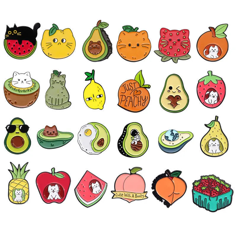 Close-up of a colourful cartoon-style fruit and letter metal brooch with a pin back on a fabric background.