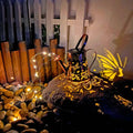 Solar-powered iron garden lamp with a tapered butterfly design emitting warm white light.