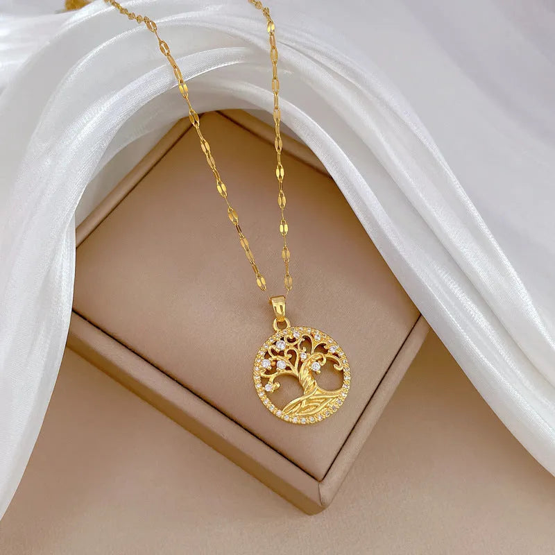 Close-up of a gold necklace with an ornate tree pendant featuring sparkling crystals and a white mother-of-pearl centre, on an adjustable chain.