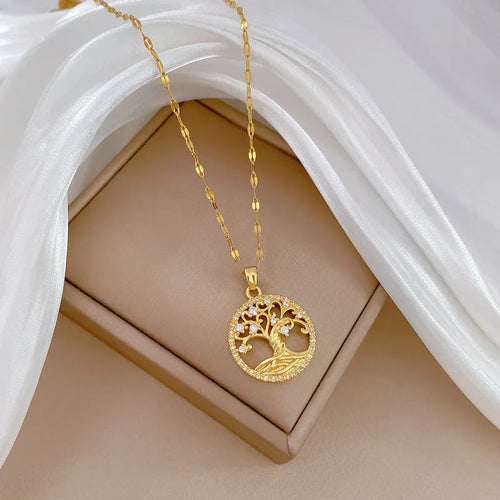 Close-up of a gold necklace with an ornate tree pendant featuring sparkling crystals and a white mother-of-pearl centre, on an adjustable chain.
