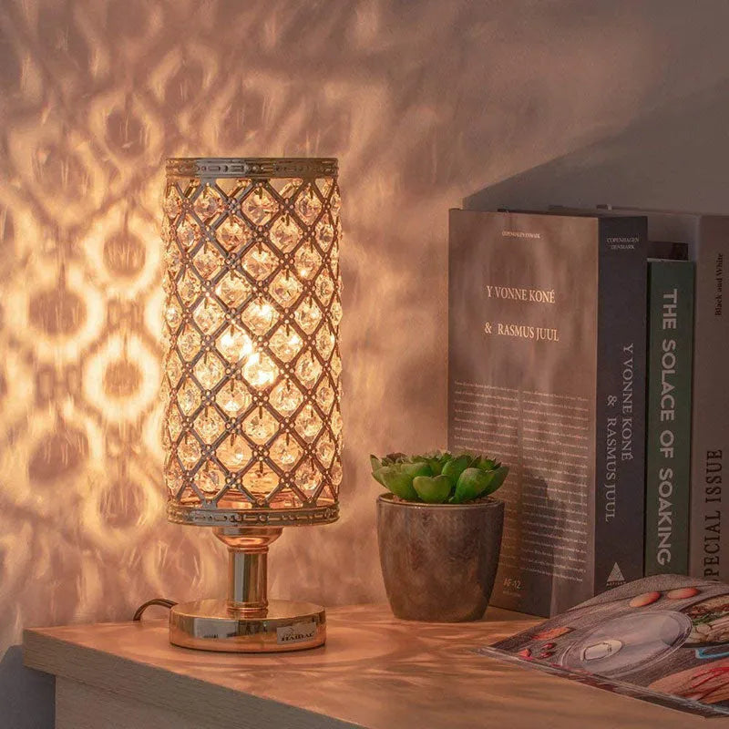 Modern crystal table lamp with gold metal base and hollow-carved crystal shade on a bedside table
