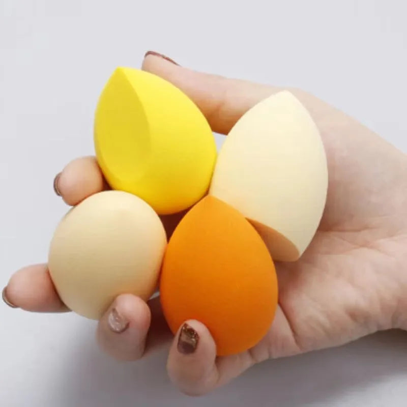 Set of seven coloured makeup sponges in different shapes on a pink background