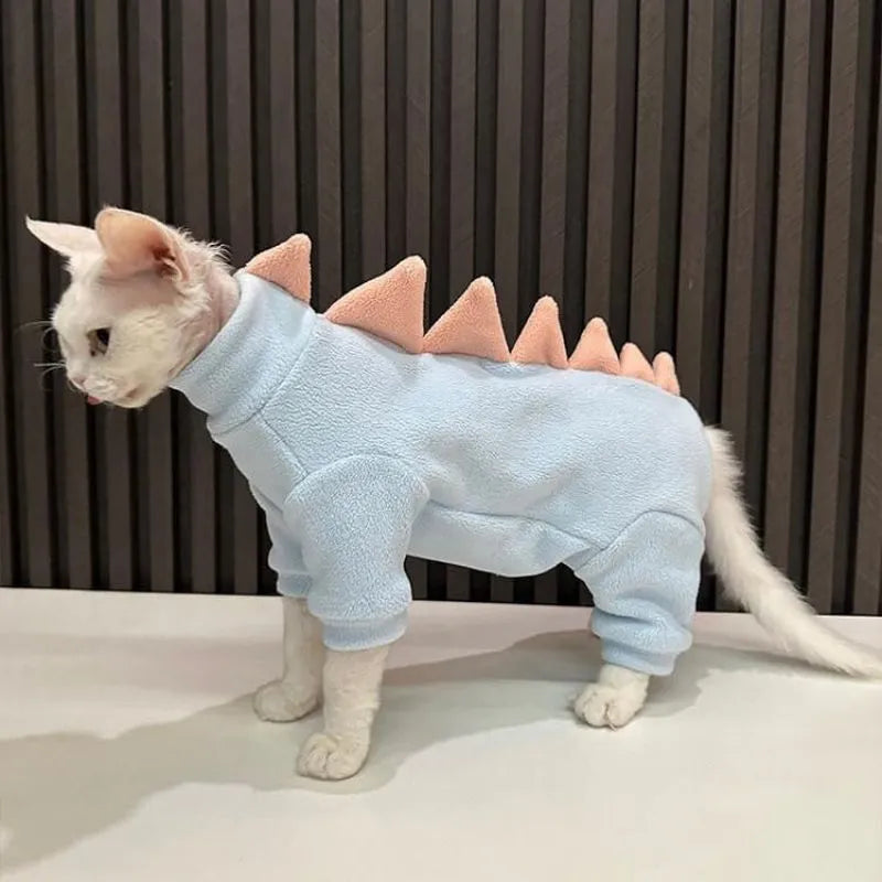 Sphynx cat wearing a green dinosaur fleece costume with a tail and back spikes.