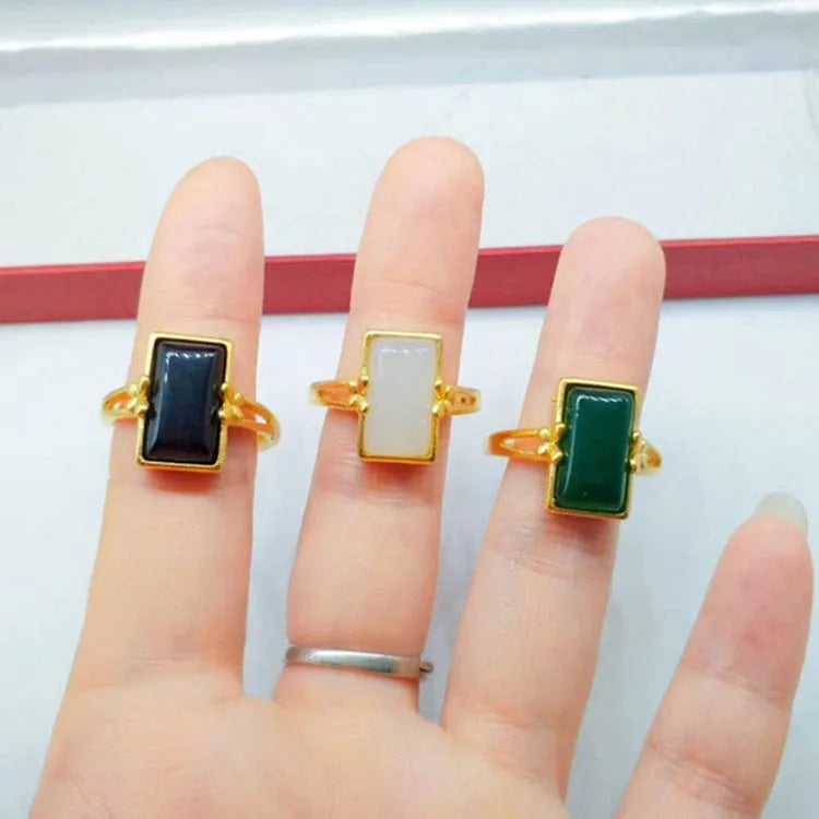 Adjustable gold-plated brass ring with a coloured gemstone inlay on a plain background.