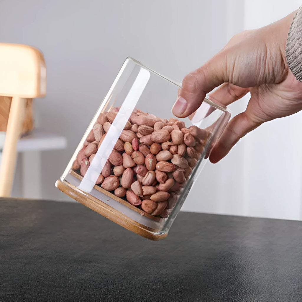 Square glass coffee bean storage jar with wooden spoon and bamboo lid on a kitchen counter