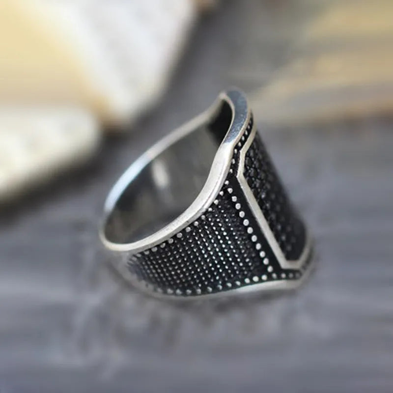A black alloy ring on a finger, showing a copper metal inlay and sparkling clear zircon stones set into the band.