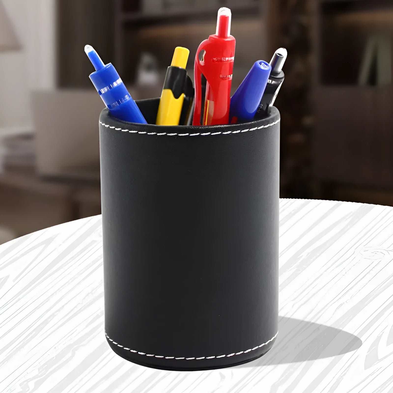 Round black leather pen container on a desk holding pens and pencils.