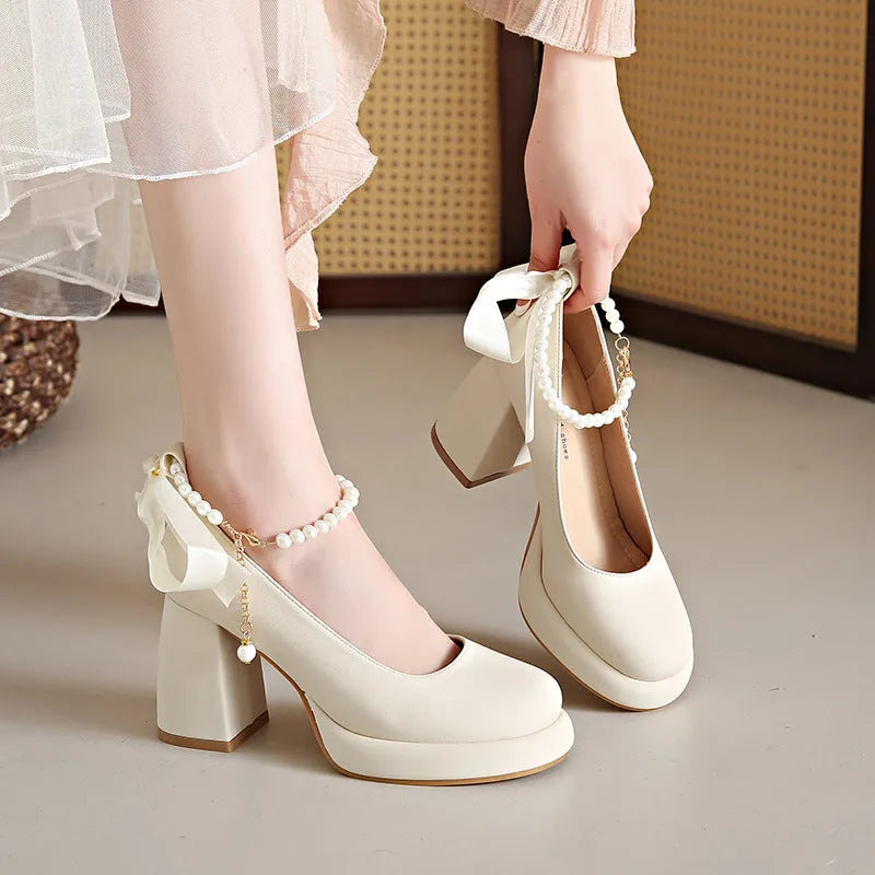 Women's beige Mary Jane shoes with chunky heel and silver ankle strap buckle on a wooden floor.