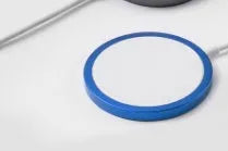 Silver metal Magsafe-compatible magnetic wireless charger for iPhone on a wooden desk.