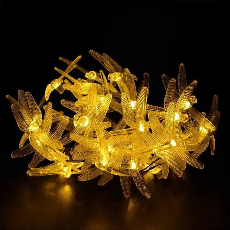 Solar powered outdoor LED string lights with dragonfly design showing warm white illumination in garden setting