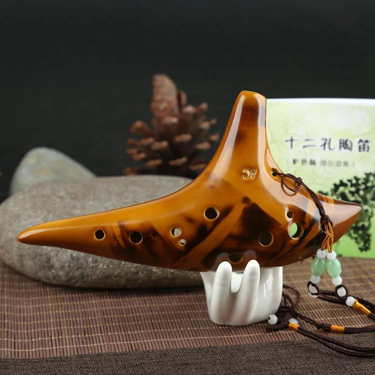 Yellow 12-hole ceramic Alto C ocarina with smoldering finish and lanyard on a surface