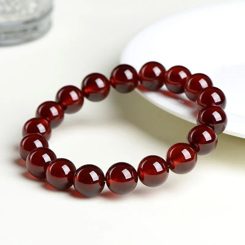 Natural Orange Red Garnet ball bead bracelet with a metal Ruyi charm on a white background.