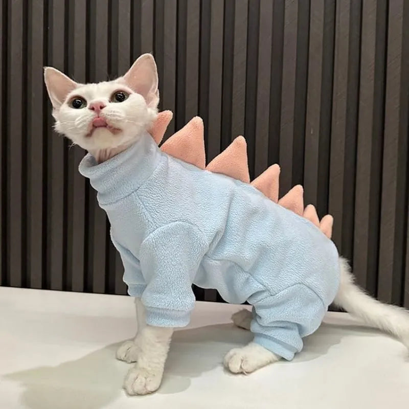 Sphynx cat wearing a green dinosaur fleece costume with a tail and back spikes.