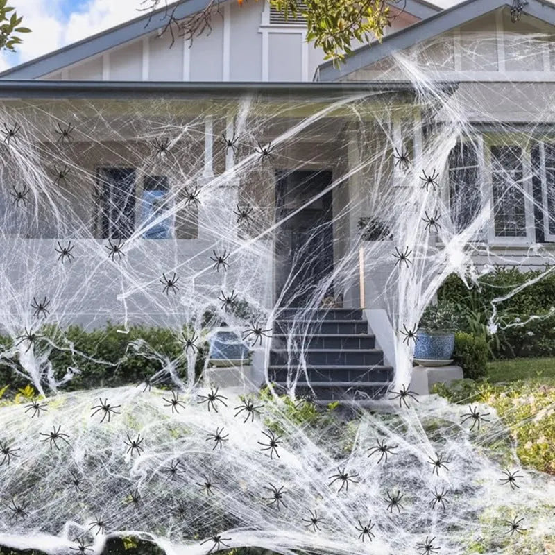 White cotton spider web Halloween decoration draped with plastic spiders on a dark background.