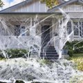 White cotton spider web Halloween decoration draped with plastic spiders on a dark background.