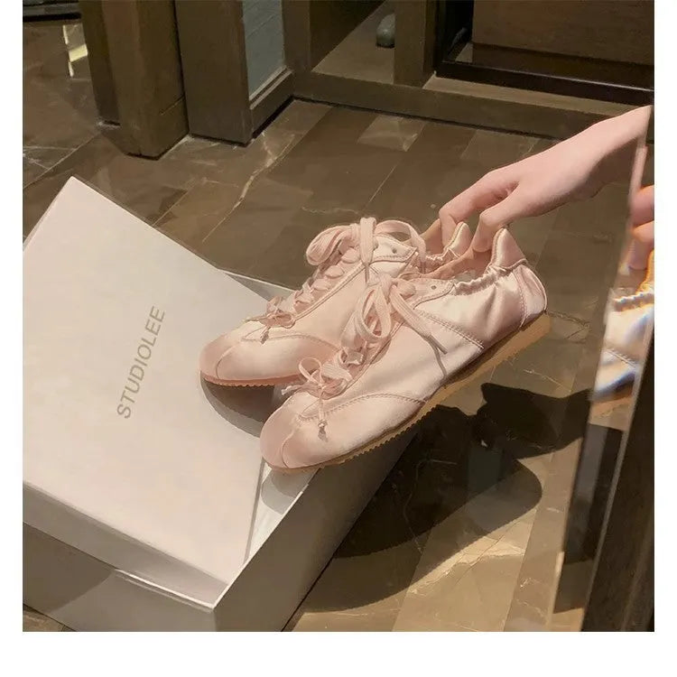 Women's champagne pink satin ballet flats with front lace-up and round toe on a white background.
