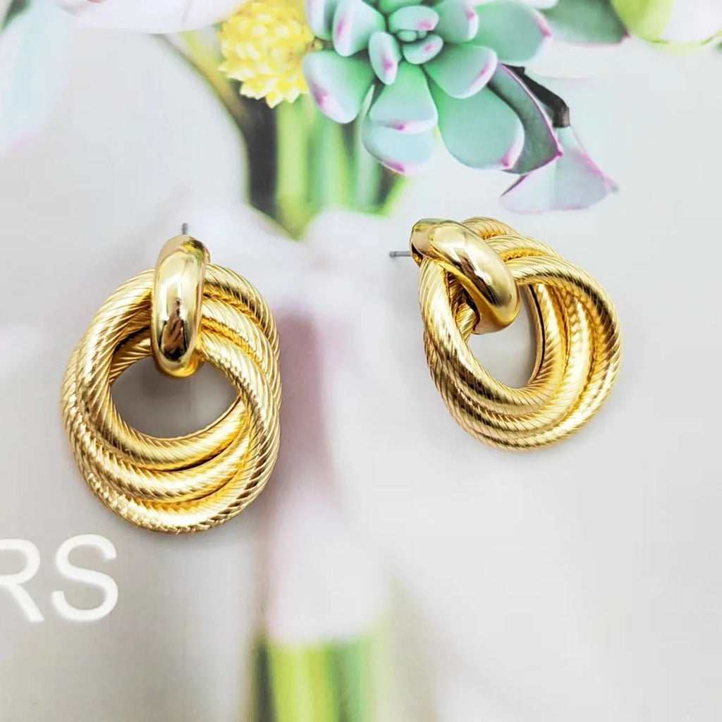 Gold metal geometric ring embossed twisted stud earrings on display
