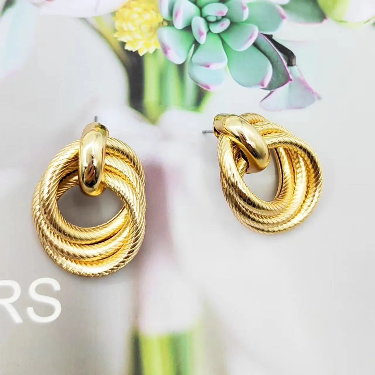 Gold metal geometric ring embossed twisted stud earrings on display