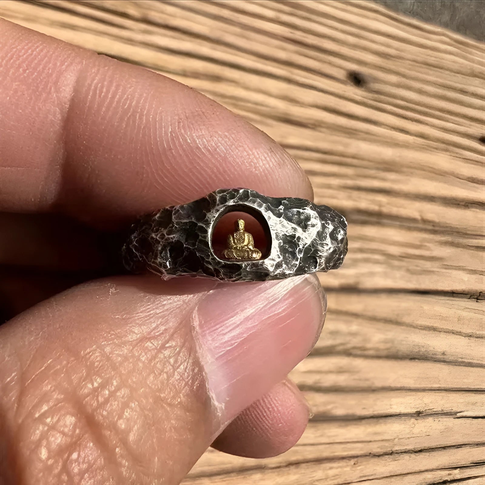 Close-up of a hand-forged copper ring with a Grotto Buddha design and rock texture.