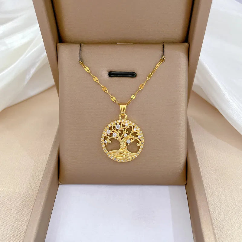 Close-up of a gold necklace with an ornate tree pendant featuring sparkling crystals and a white mother-of-pearl centre, on an adjustable chain.