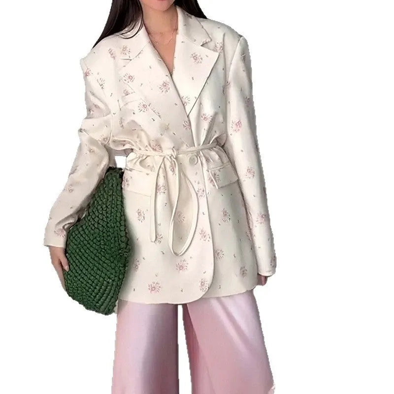 White floral print suit jacket with a lace-up detail at the waist on a hanger.