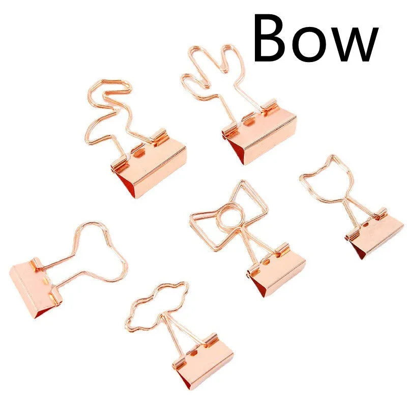 Gold metal alloy paper clip with decorative bow shape top on white background.