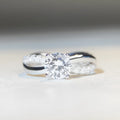 Silver ring with twisted geometric band and a 1 karat moissanite in a four-claw setting.