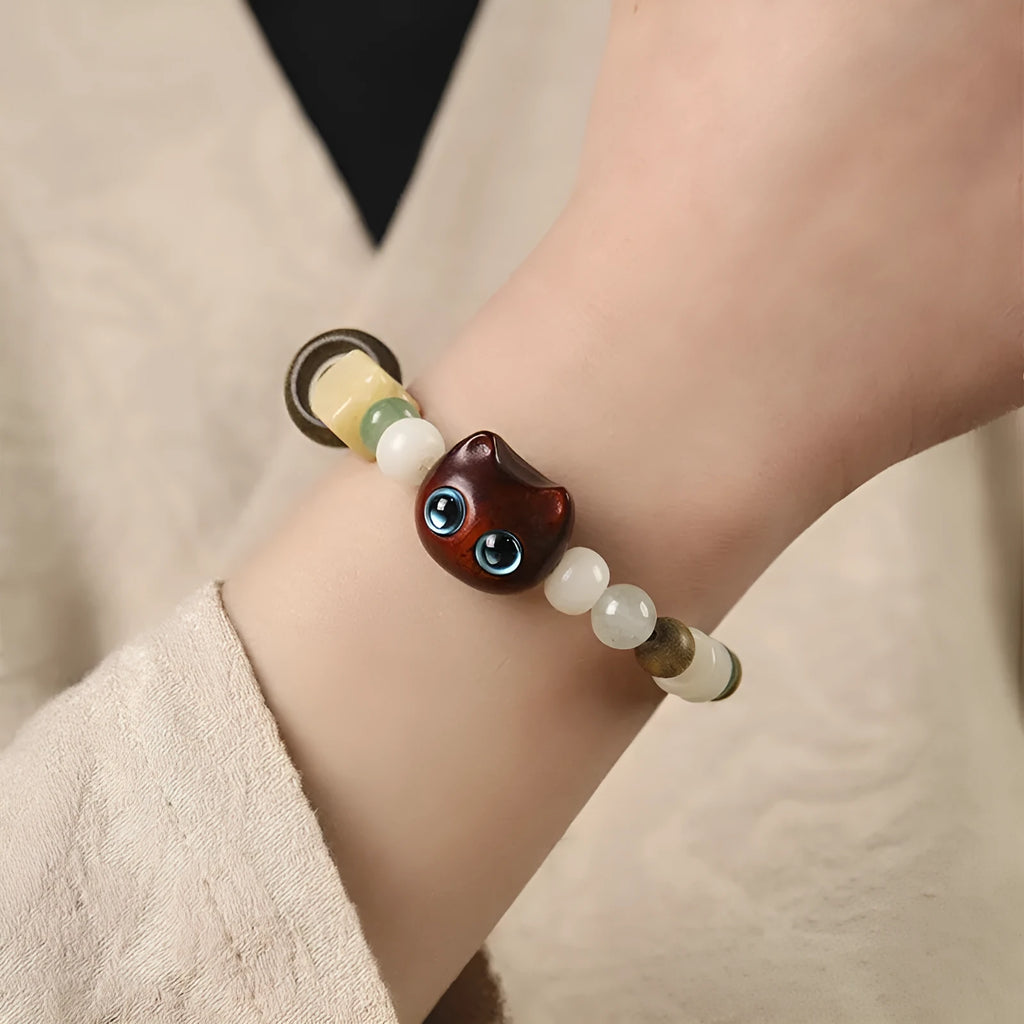 Beaded bracelet with a cube sugar cat's paw charm in guajacwood or ebony, featuring jade beads and a choice of yellow or blue eyes.