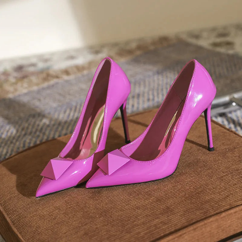Women's pink patent leather pointed toe stiletto heels with an ankle buckle strap on a white background.