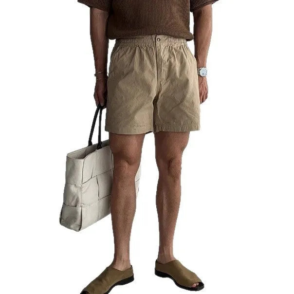 A pair of loose-fitting cotton sports shorts in khaki colour on a white background.