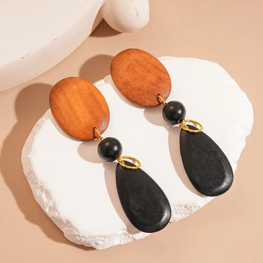 Wooden drop earrings with an ellipse shape in silver, brown, and black colours, showing manual craftsmanship.